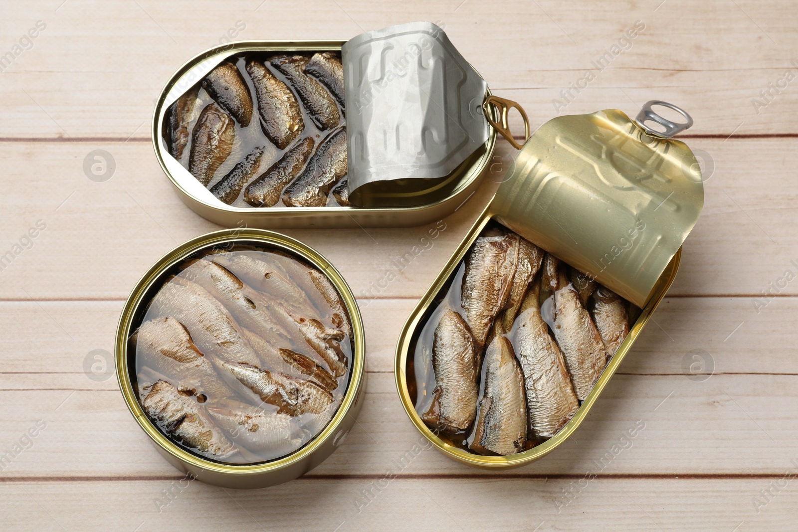 Photo of Tasty sprats in tin cans on wooden table, top view