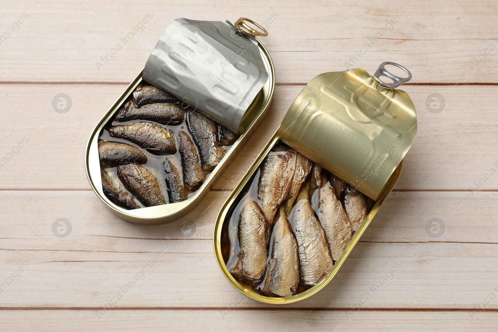 Photo of Tasty sprats in tin cans on wooden table, top view