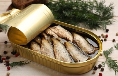 Photo of Tasty sprats in tin can, dill and peppercorns on wooden table, closeup