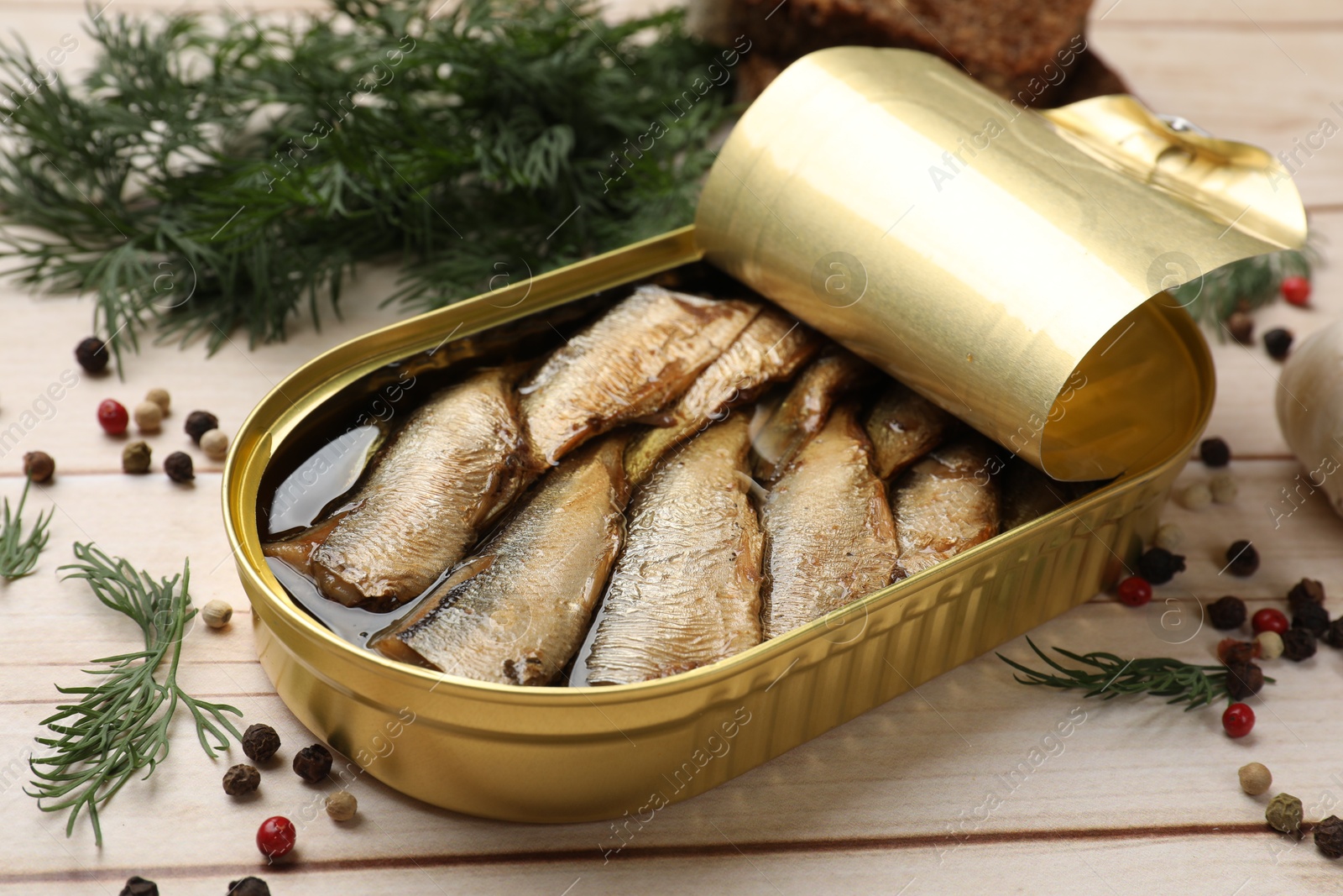 Photo of Tasty sprats in tin can, dill and peppercorns on wooden table, closeup