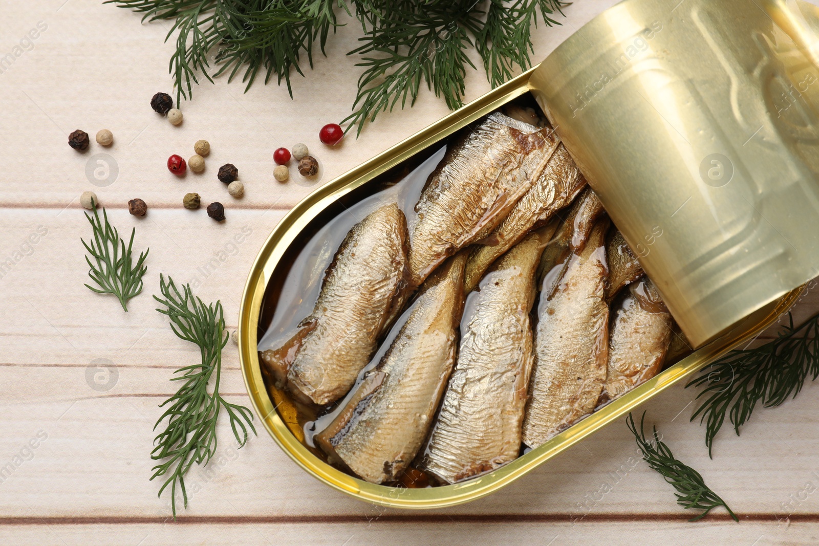 Photo of Tasty sprats in tin can, dill and peppercorns on wooden table, top view