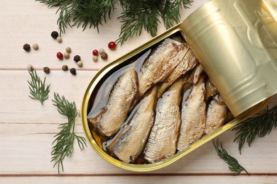 Photo of Tasty sprats in tin can, dill and peppercorns on wooden table, top view