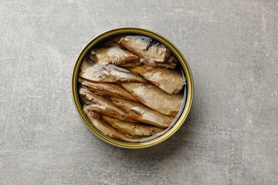 Photo of Tasty sprats in tin can on grey textured table, top view