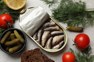 Photo of Tasty sprats in tin can served on grey textured table, flat lay