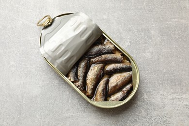 Tasty sprats in tin can on grey textured table, top view