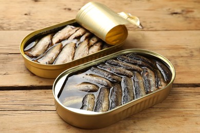 Tasty sprats in tin cans on wooden table, closeup