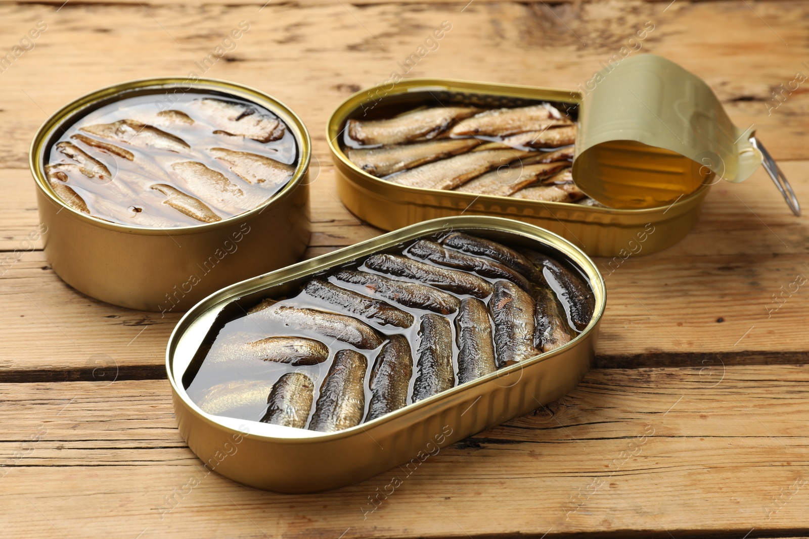 Photo of Tasty sprats in tin cans on wooden table, closeup