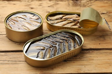 Tasty sprats in tin cans on wooden table, closeup