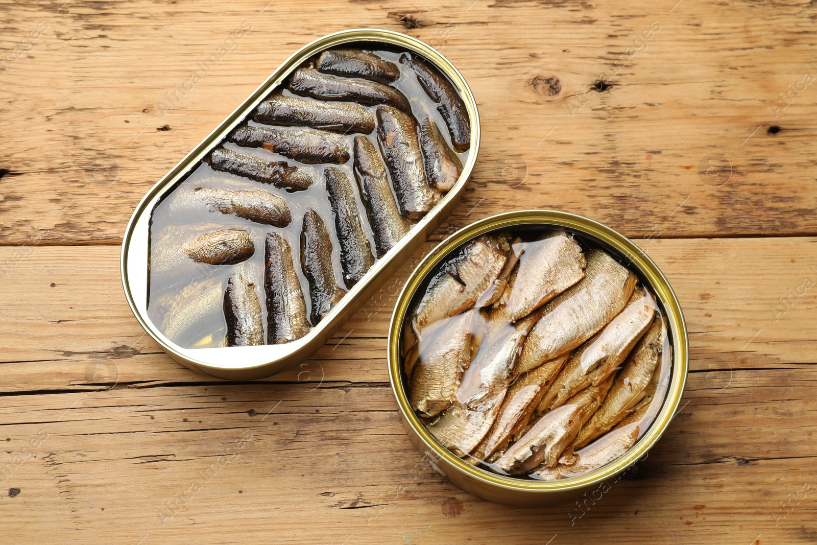 Photo of Tasty sprats in tin cans on wooden table, flat lay