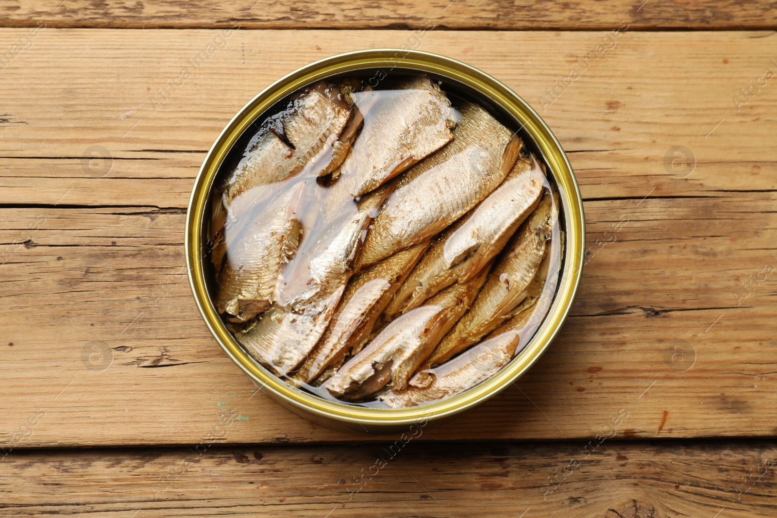 Photo of Tasty sprats in tin can on wooden table, top view