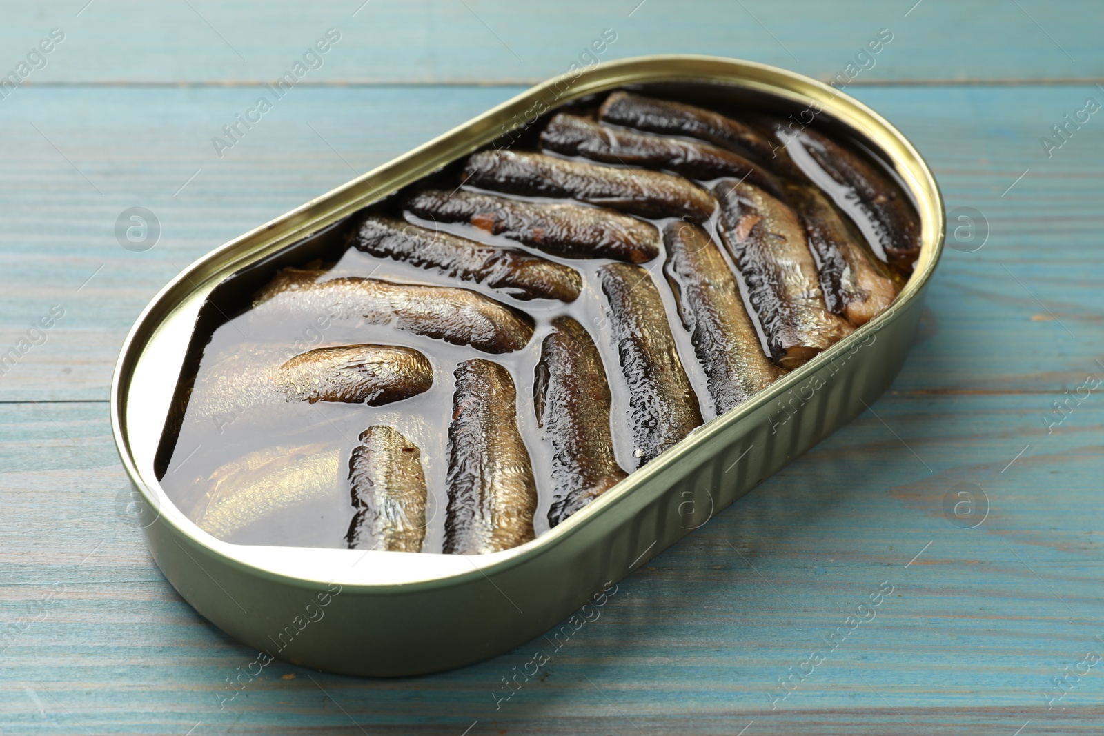 Photo of Tasty sprats in tin can on light blue wooden table, closeup