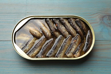 Tasty sprats in tin can on light blue wooden table, top view