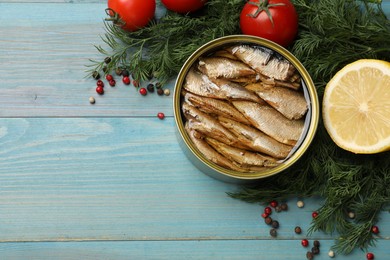 Tasty sprats in tin can served on light blue wooden table, flat lay. Space for text