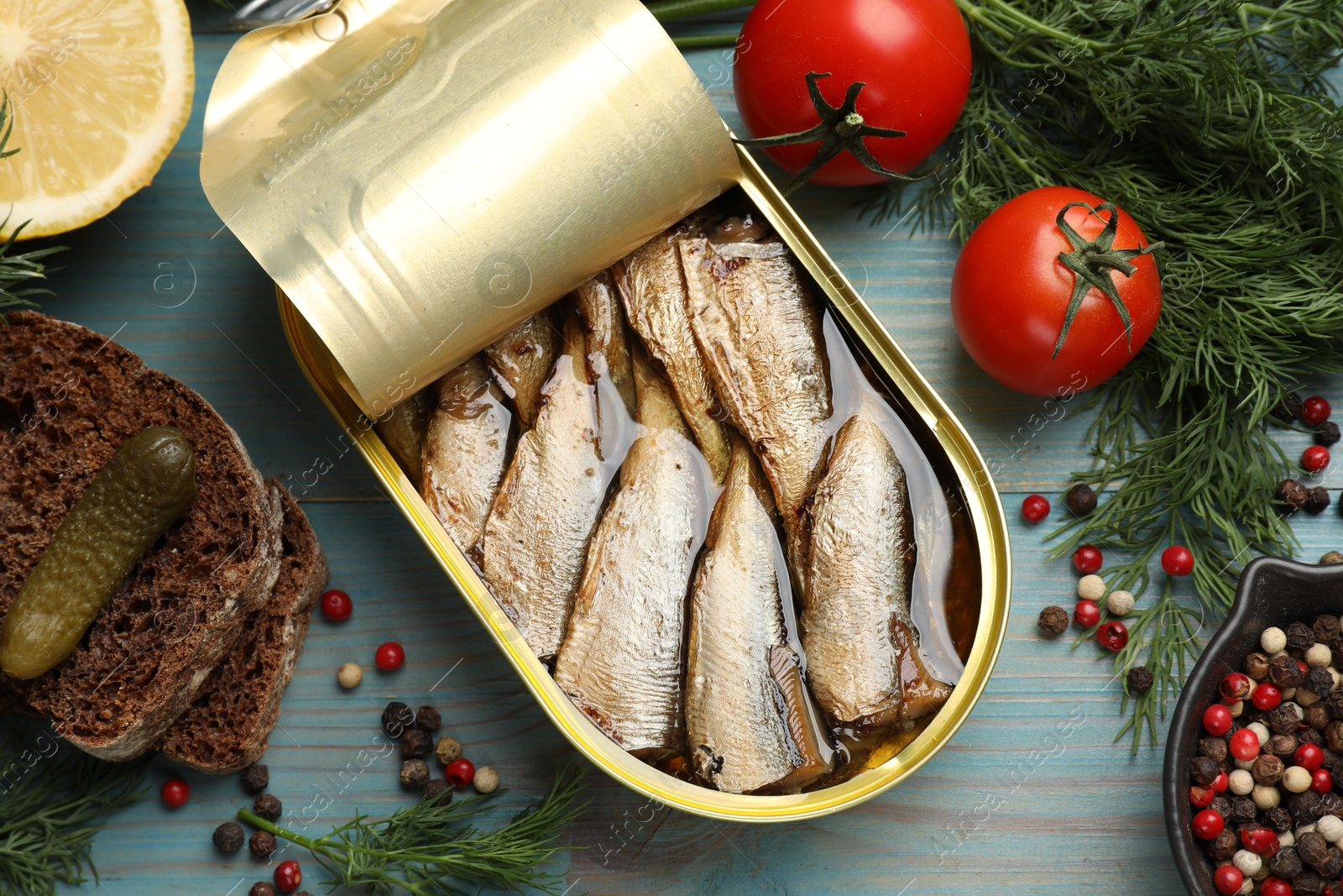 Photo of Tasty sprats in tin can served on light blue wooden table, flat lay