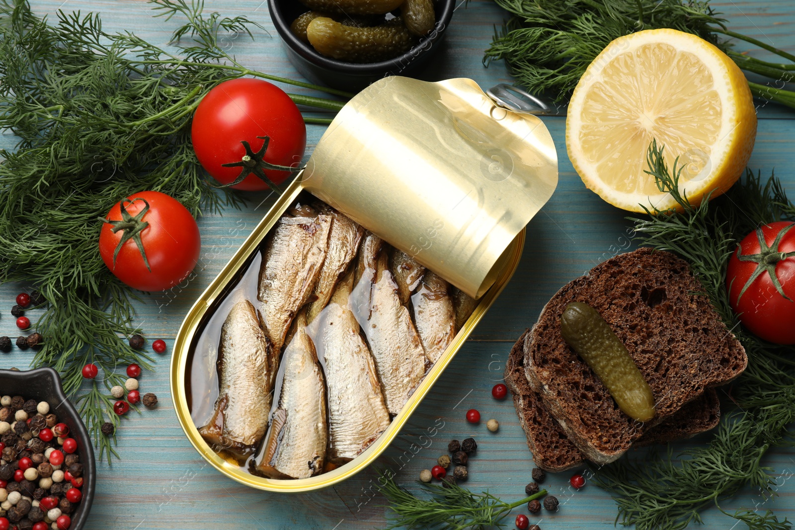 Photo of Tasty sprats in tin can served on light blue wooden table, flat lay