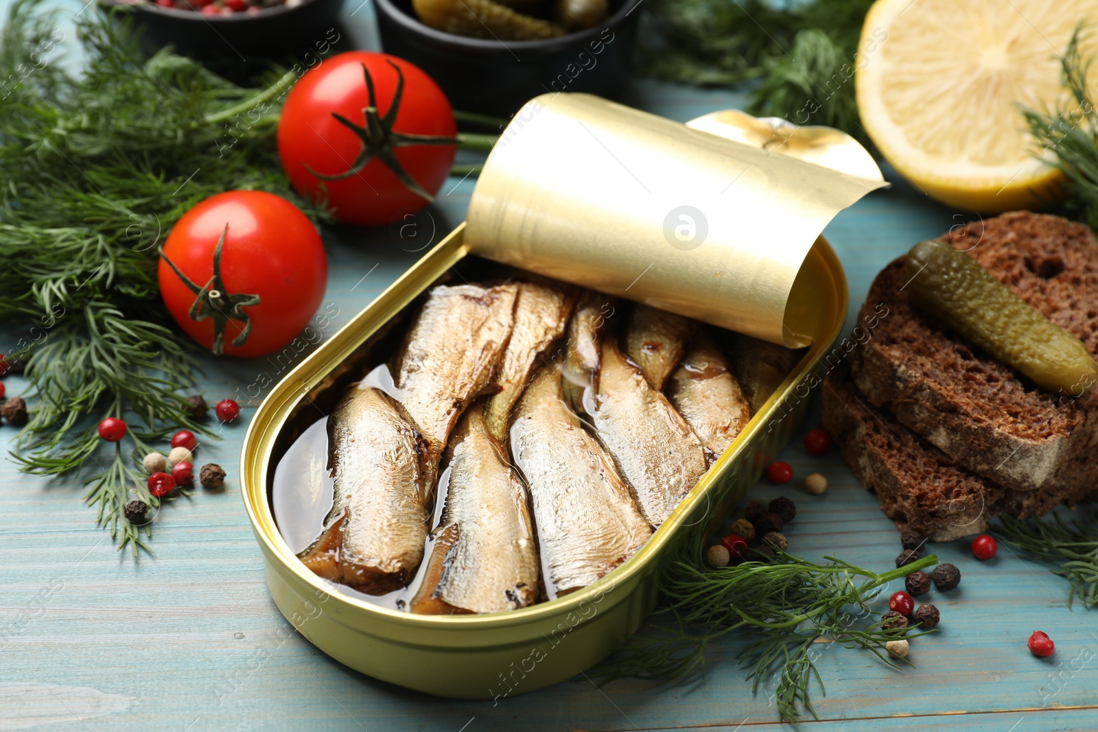 Photo of Tasty sprats in tin can served on light blue wooden table, closeup