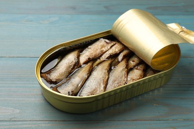 Photo of Tasty sprats in tin can on light blue wooden table, closeup