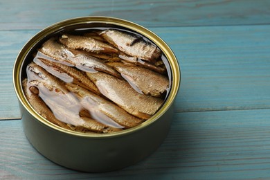 Photo of Tasty sprats in tin can on light blue wooden table, closeup