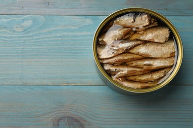 Tasty sprats in tin can on light blue wooden table, top view. Space for text