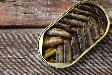 Tasty sprats in tin can on wooden table, top view