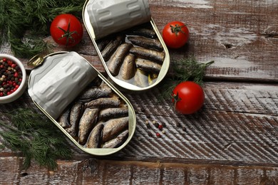 Photo of Tasty sprats in tin cans served on wooden table, flat lay