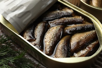 Tasty sprats in tin can with dill on wooden table, closeup