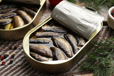 Tasty sprats in tin cans with dill on wooden table, closeup