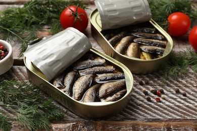 Photo of Tasty sprats in tin cans with fresh dill and tomatoes on wooden table