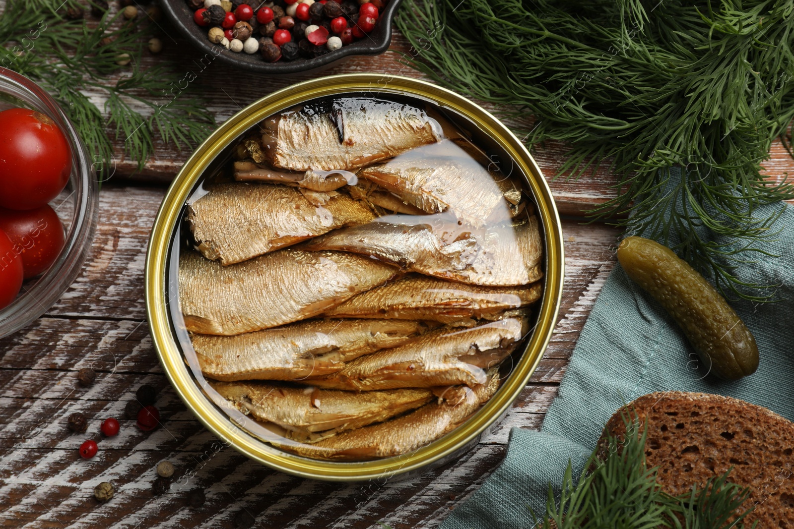 Photo of Tasty sprats in tin can served on wooden table, flat lay