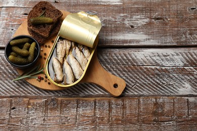 Photo of Tasty sprats in tin can served on wooden table, top view. Space for text