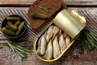 Tasty sprats in tin can served on wooden table, flat lay