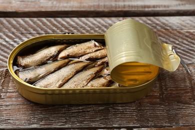 Tasty sprats in tin can on wooden table, closeup