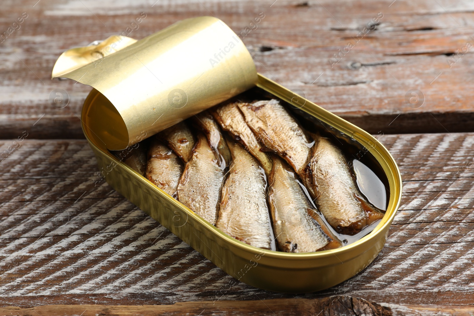 Photo of Tasty sprats in tin can on wooden table, closeup