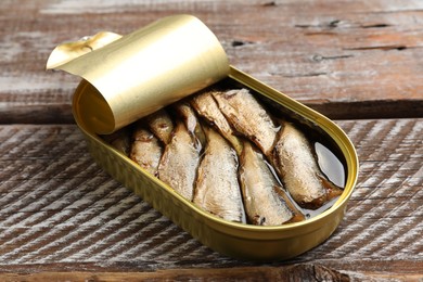 Tasty sprats in tin can on wooden table, closeup