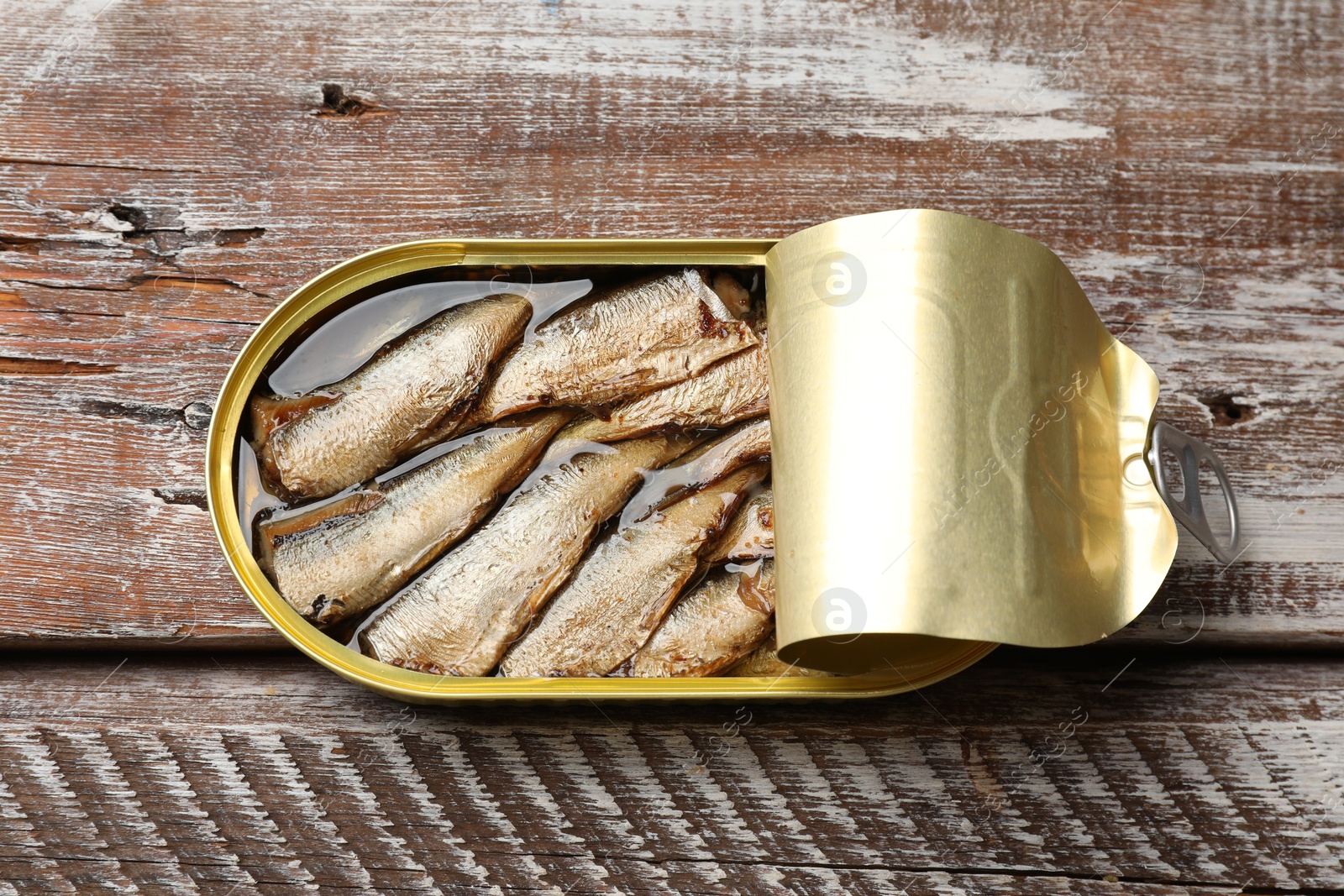 Photo of Tasty sprats in tin can on wooden table, top view