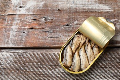 Photo of Tasty sprats in tin can on wooden table, top view. Space for text