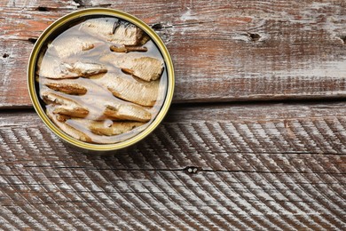 Photo of Tasty sprats in tin can on wooden table, top view. Space for text