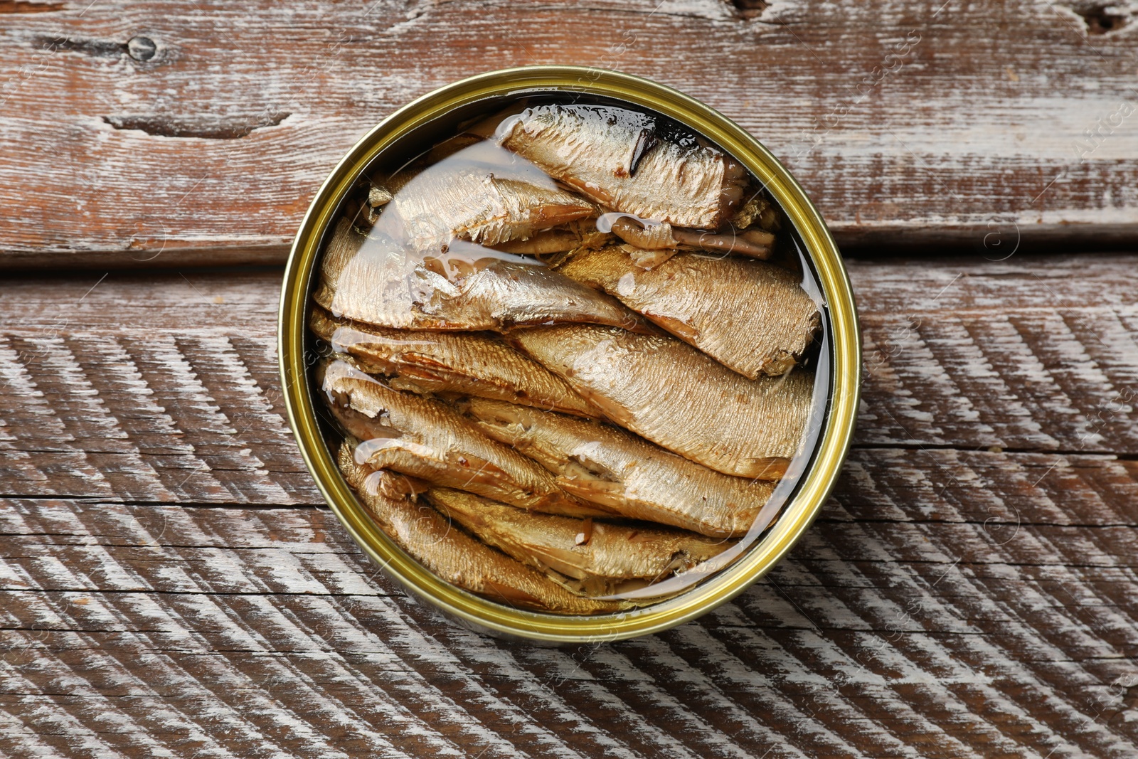 Photo of Tasty sprats in tin can on wooden table, top view