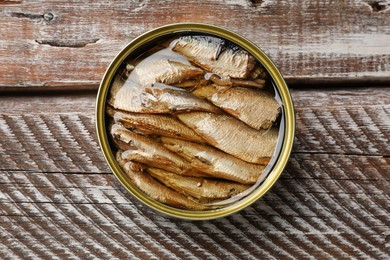 Tasty sprats in tin can on wooden table, top view