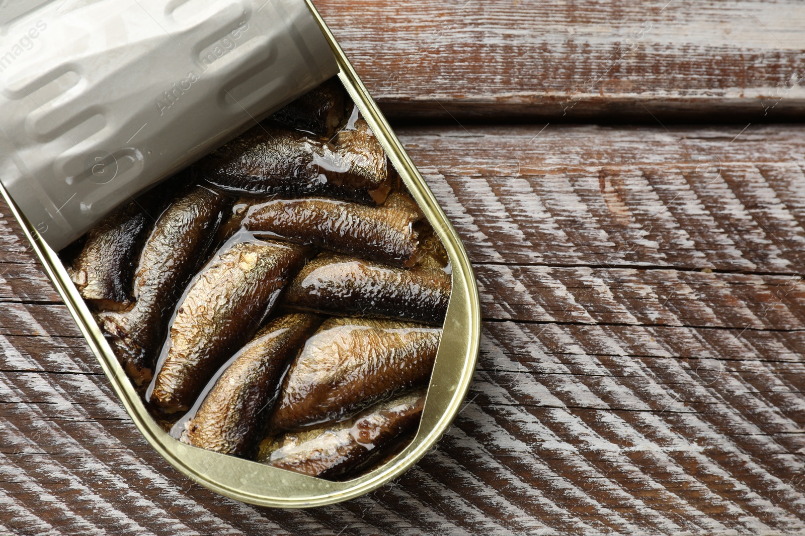 Photo of Tasty sprats in tin can on wooden table, top view. Space for text