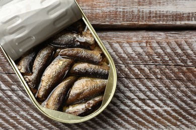 Tasty sprats in tin can on wooden table, top view. Space for text