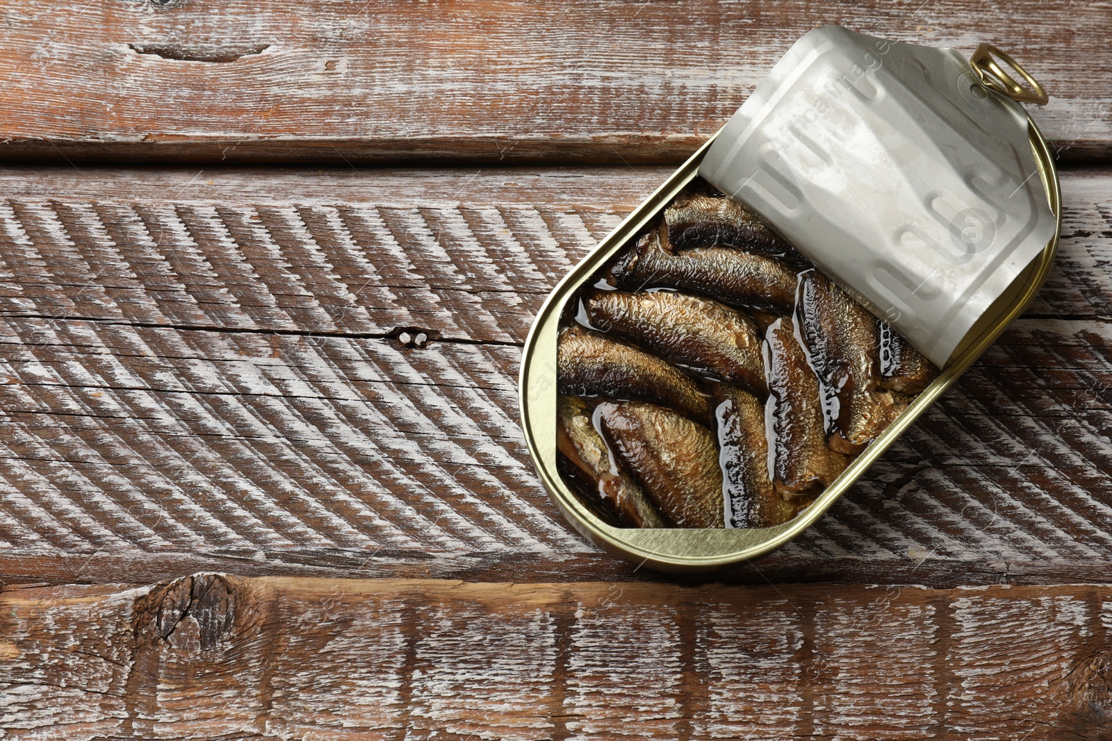 Photo of Tasty sprats in tin can on wooden table, top view. Space for text