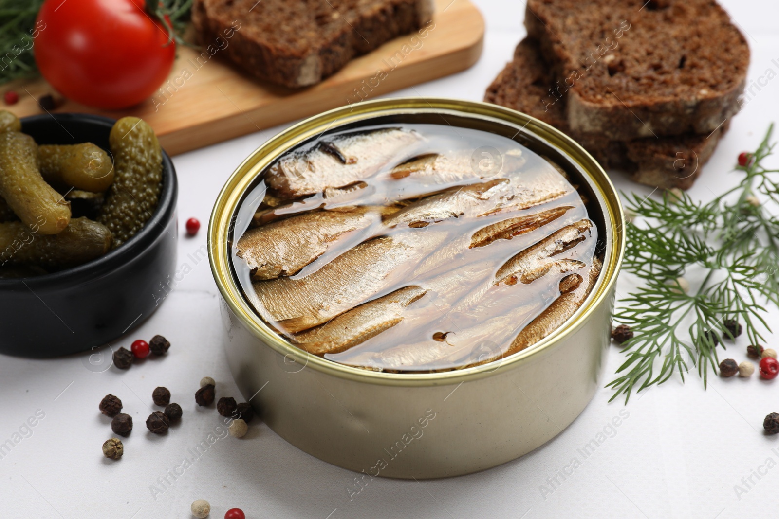 Photo of Tasty sprats in tin can served on white table, closeup