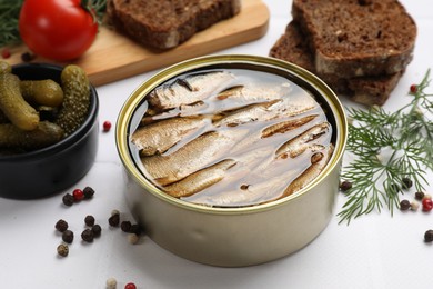 Photo of Tasty sprats in tin can served on white table, closeup