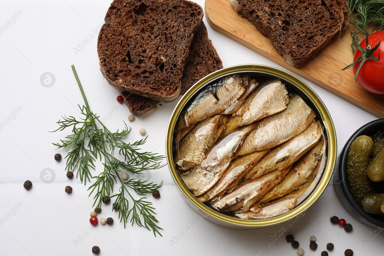 Photo of Tasty sprats in tin can served on white table, flat lay