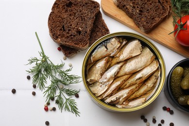 Tasty sprats in tin can served on white table, flat lay