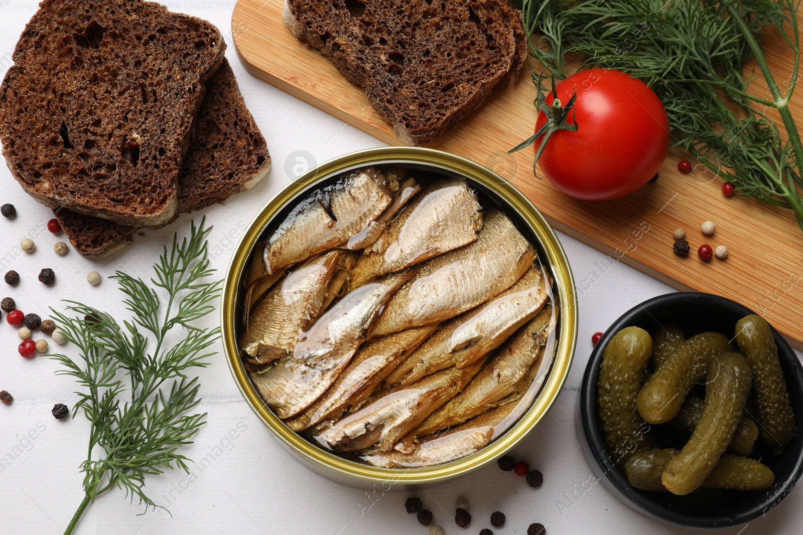 Photo of Tasty sprats in tin can served on white table, flat lay