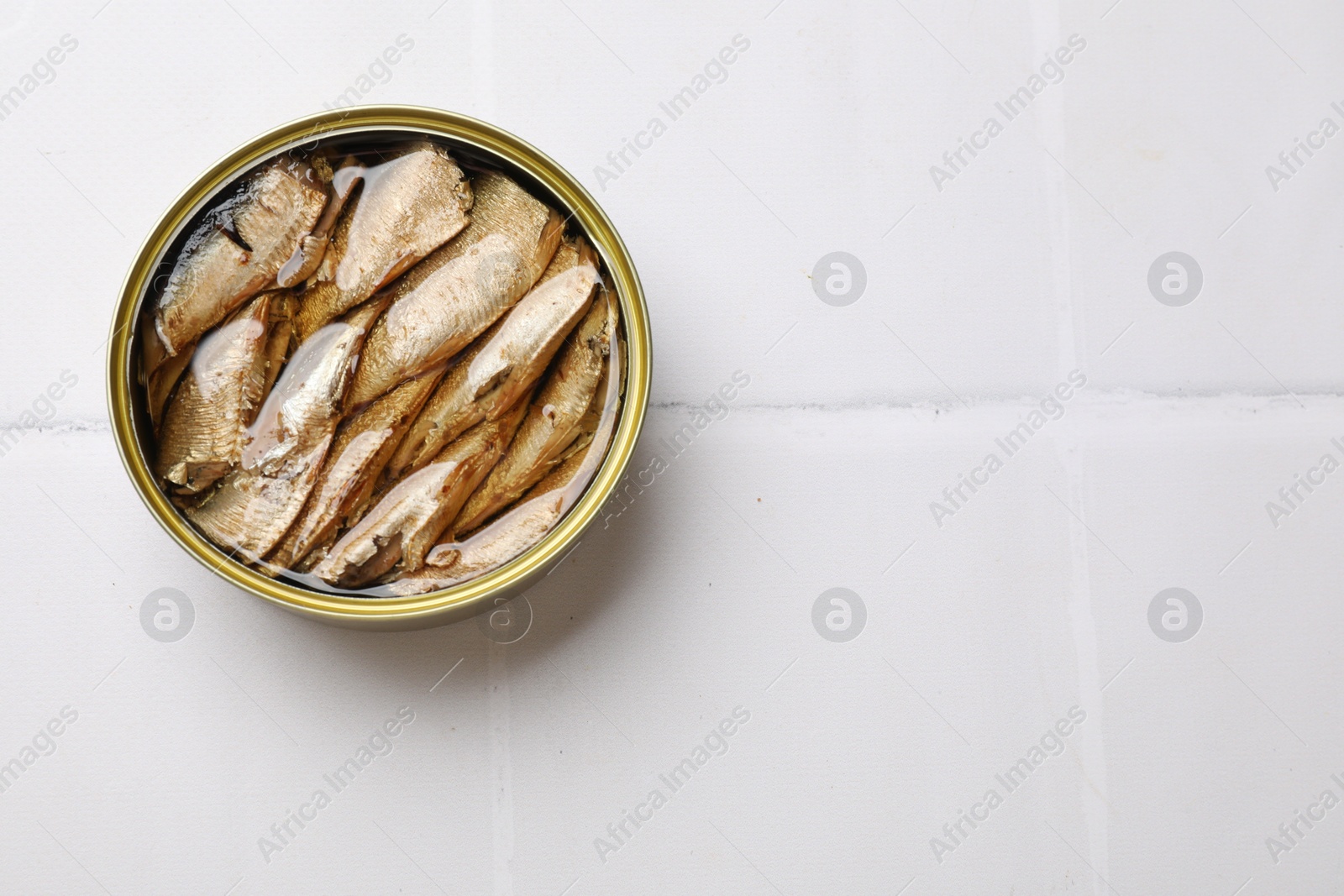 Photo of Tasty sprats in tin can on white tiled table, top view. Space for text