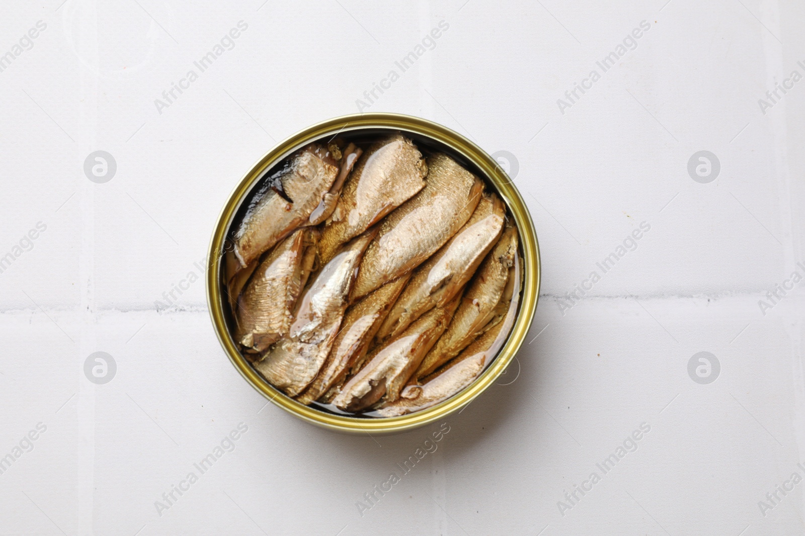 Photo of Tasty sprats in tin can on white tiled table, top view