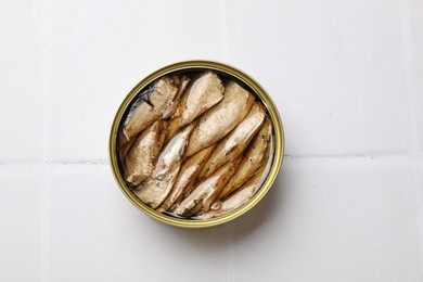 Tasty sprats in tin can on white tiled table, top view